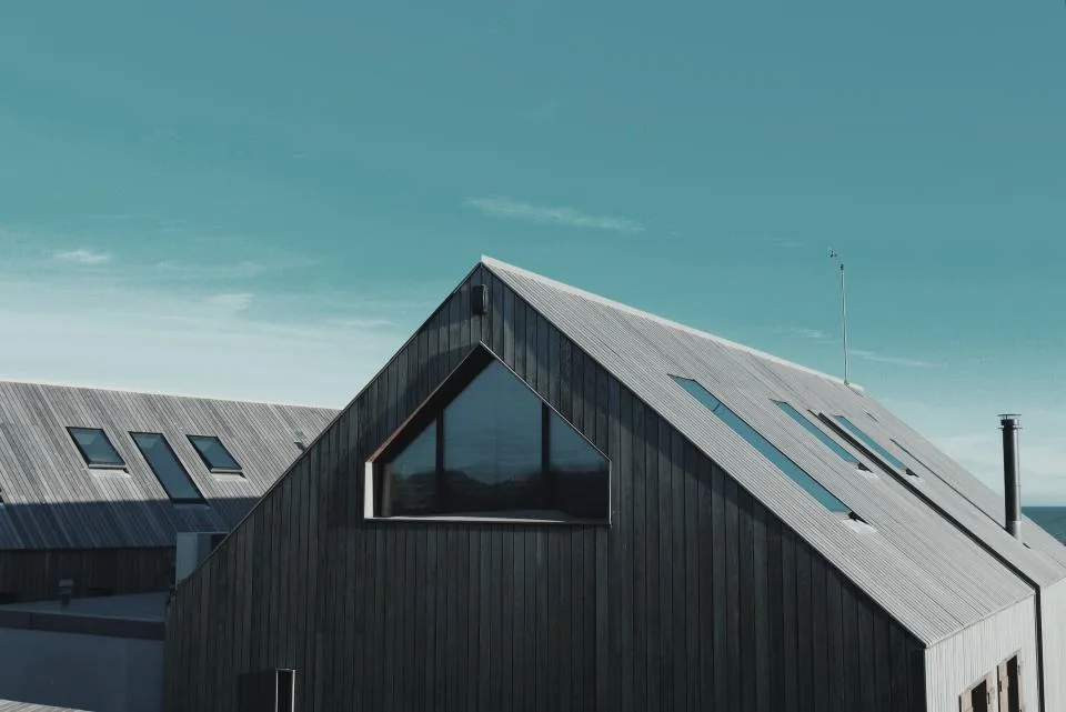 Maison à pignon en bardage bois sombre sous un ciel clair