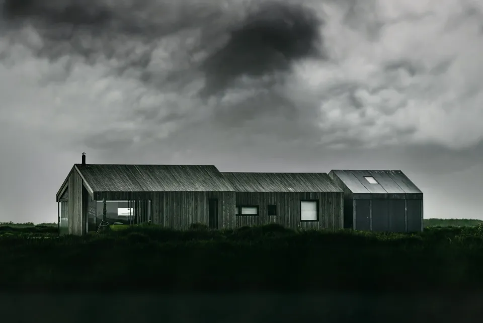Longue maison en bois sombre posée dans un pré sous un ciel d'orage