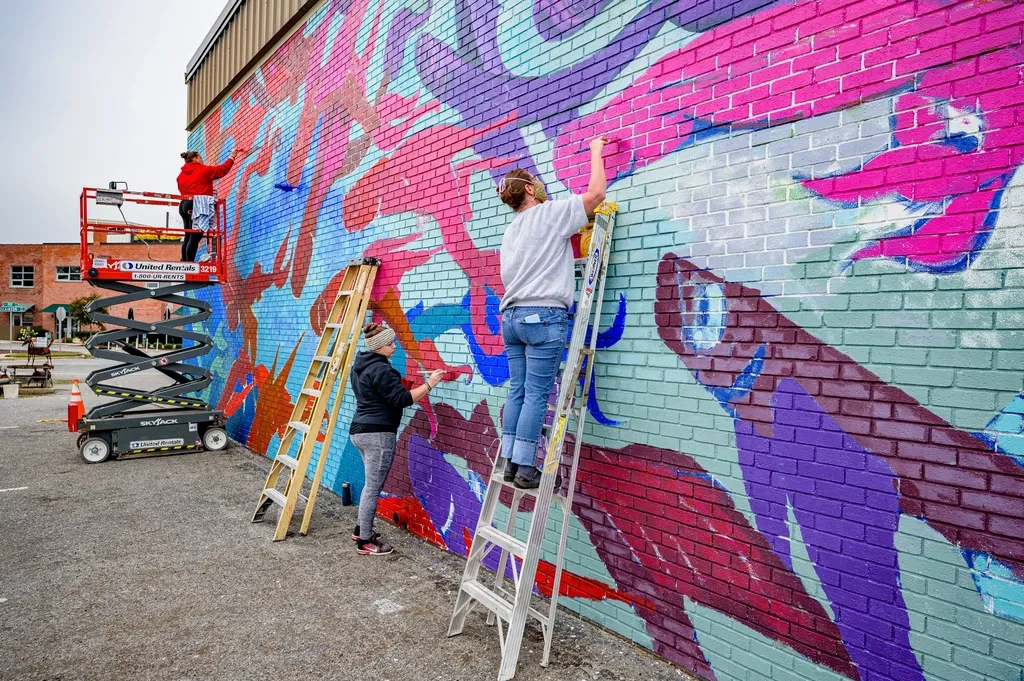 Des habitants peignent une grande fresque colorée sur un mur de briques