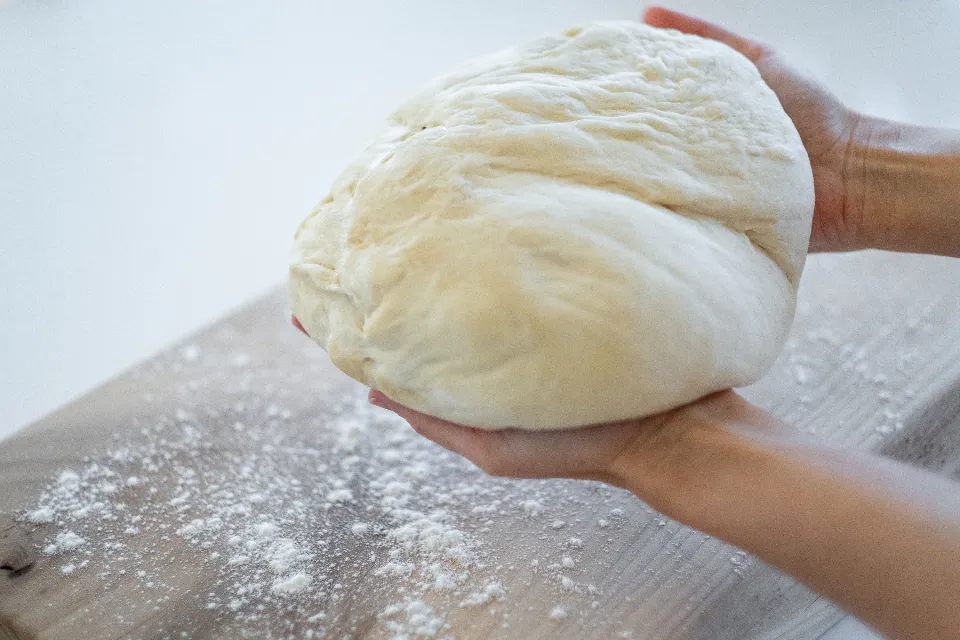 Mains qui façonnent une boule de pâte sur un plan fariné