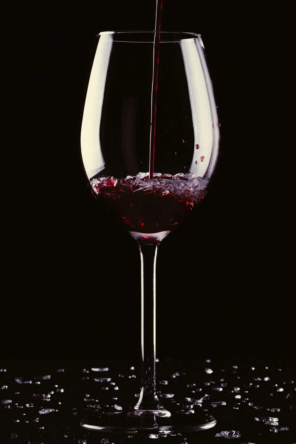 Vin rouge versé dans un verre à pied sur fond noir