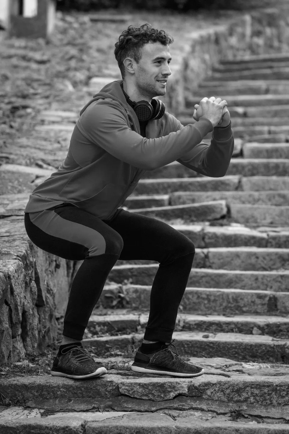 Sportif en tenue d'entraînement faisant un squat sur des marches en pierre