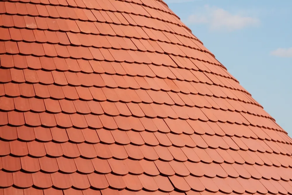 Pan de toiture neuf en tuiles plates rouges sous un ciel bleu