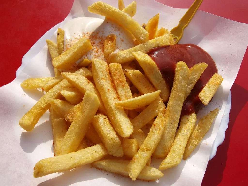 Cornet de frites dorées avec une sauce, servi sur un papier blanc