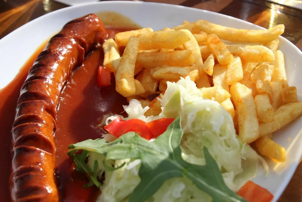 Saucisse grillée nappée de sauce, frites et crudités