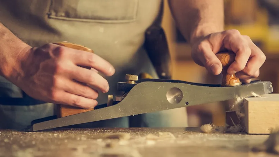 Mains d'un menuisier rabotant une planche de bois à l'établi