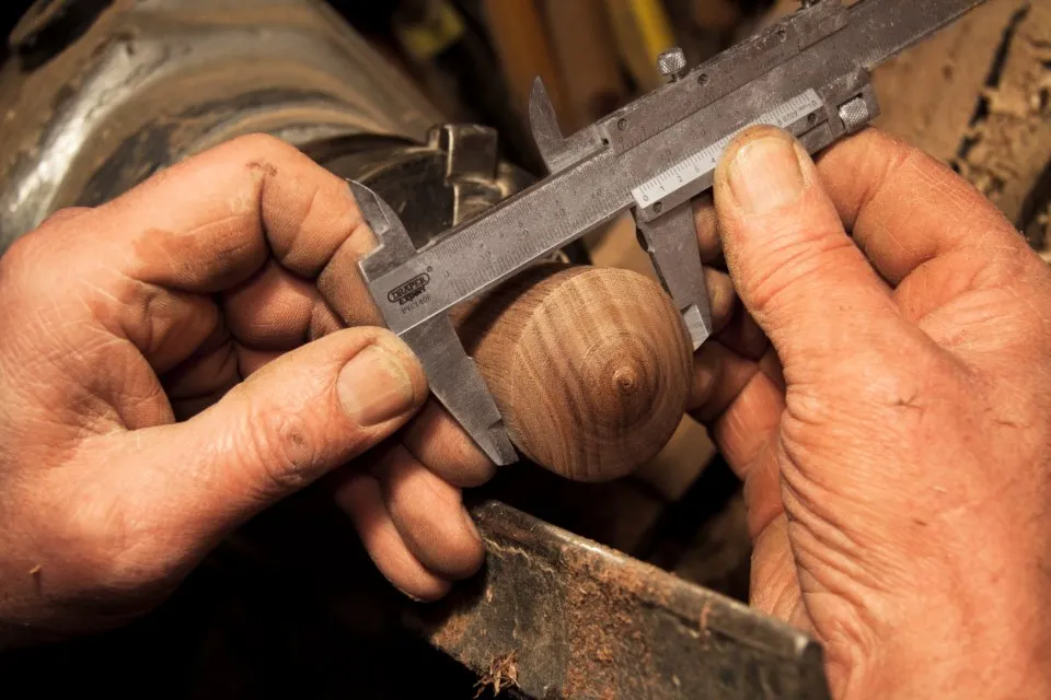 Mains mesurant une pièce de bois tournée au pied à coulisse