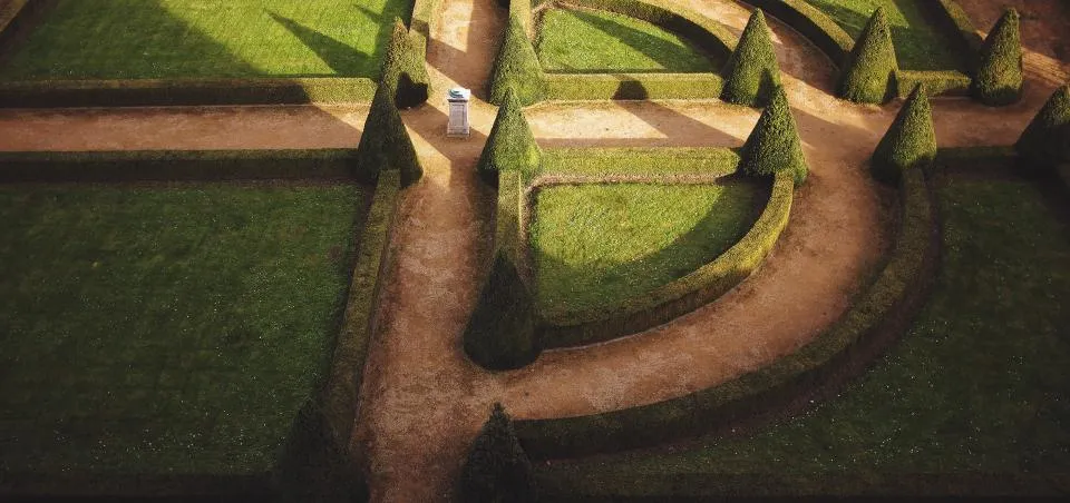 Vue plongeante sur un jardin structuré d'allées en terre battue et de haies basses