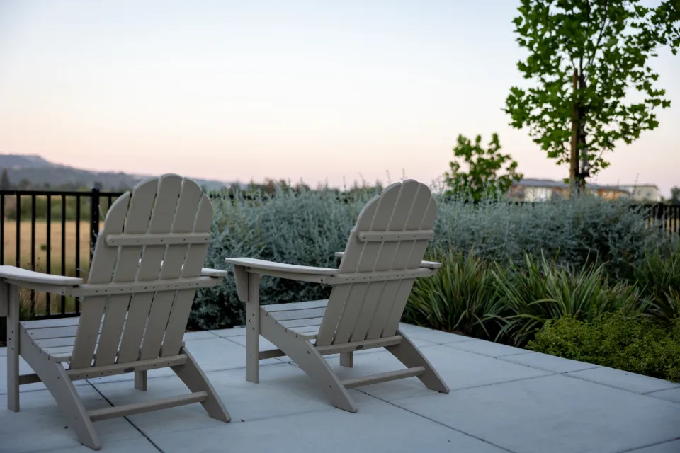 Terrasse en dalles claires avec deux fauteuils de jardin, bordée de graminées et de lavandes