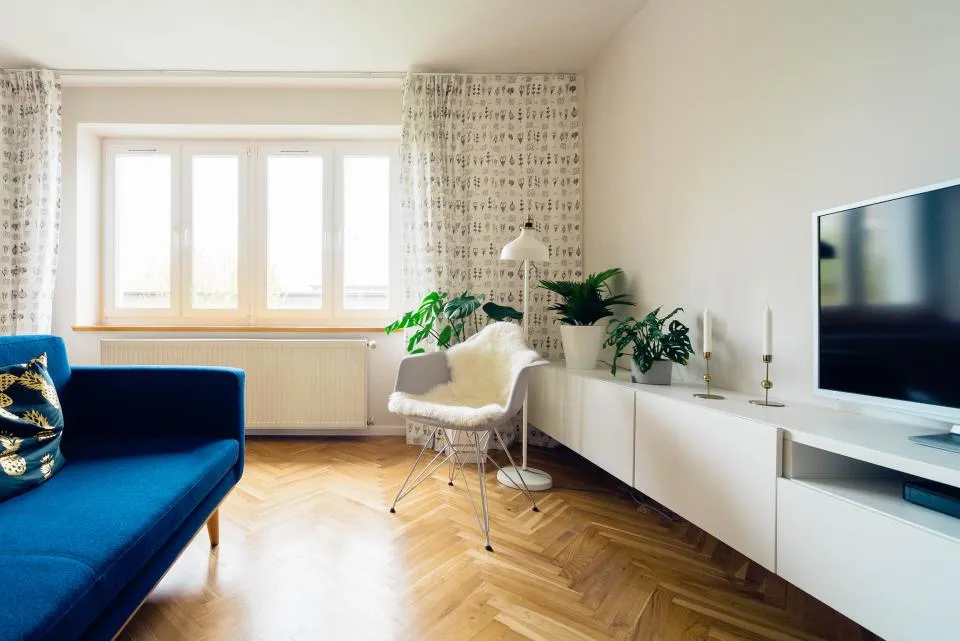 Salon aux murs blancs avec canapé bleu et parquet en chevrons