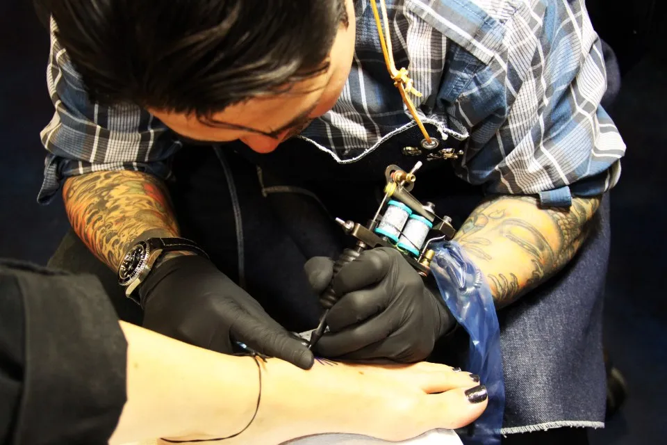 Tatoueur ganté de bleu en pleine séance sur un avant-bras